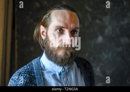 Mode Portrait einer Nachdenklich, bärtiger Mann mit einem blauen Hemd und Blau Strickjacke auf grauem Hintergrund. Rücksichtnahme Konzept Stockfoto
