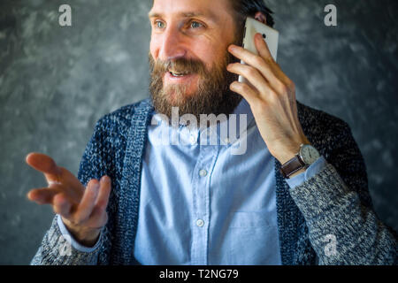Glücklich lächelnde Bärtiger Mann sprechen am Telefon und Gestikuliert während eines Gesprächs. Offene und freundliche Kommunikation mit ein angenehmer Gesprächspartner. Gute Nachrichten Stockfoto