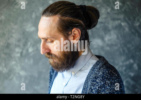 Mode Portrait einer Nachdenklich, bärtiger Mann mit einem blauen Hemd und Blau Strickjacke auf grauem Hintergrund. Rücksichtnahme Konzept Stockfoto