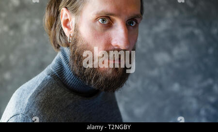 Mode Portrait von bärtiger Mann mit einem gleichgültigen Hochmütig in Grau hohe Pullover auf grauem Hintergrund. Stockfoto