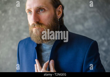 Mode Portrait von bärtigen Mann in Grau hohe Pullover Stellring im blauen Anzug Blazer. Stockfoto