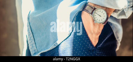 Nahaufnahme der Männer Zubehör elegante Armbanduhren. Die Hand in der Tasche. Shirt Ärmel hochgekrempelt. Informelle Casual Konzept Verschleiß Stockfoto