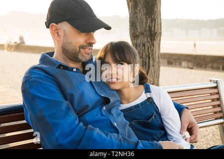 Vater und Tochter sitzen auf einer Bank an der Uferpromenade in einem guten Gespräch an einem sonnigen Tag Stockfoto