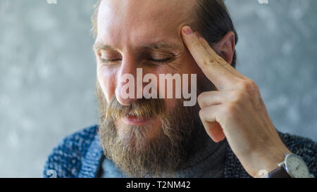 Ein Angriff von starken Kopfschmerzen in einem stilvollen Bärtiger Mann im Büro. Symptom Krankheit Hintergrund Konzept Stockfoto