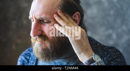 Ein Angriff von starken Kopfschmerzen in einem stilvollen Bärtiger Mann im Büro. Symptom Krankheit Hintergrund Konzept Stockfoto