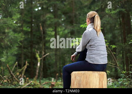 Eine Frau entspannt auf einem Baumstamm in einem Wald Stockfoto