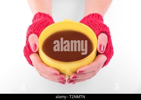 Weibliche Hände in rot Handschuhe halten eine gelbe Tasse trinken Stockfoto