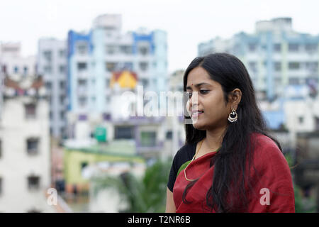 Schönen indischen Bengali Dame im roten Sari stehend auf der Dachterrasse mit urbanen Landschaft Hintergrund Stockfoto