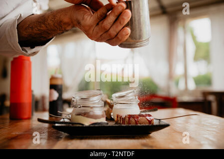 Koch streuen Puderzucker auf Dessert Stockfoto