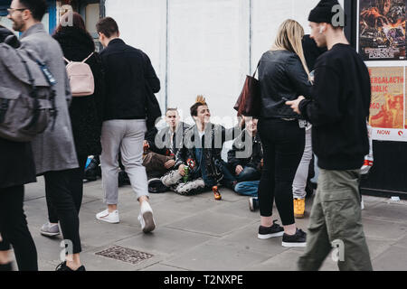 London, UK, 23. März 2019: Menschen zu Fuß Vergangenheit Punkrocker sitzen auf einer Straße in Camden Town, London, ein Bereich für seinen Markt berühmt und Nachtleben ein Stockfoto