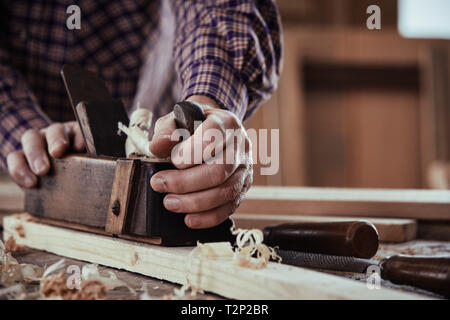 Tischler oder Schreiner Hobeln ein Brett aus Holz Glättung der Oberfläche in der Nähe zu sehen, auf seinen Händen und das Werkzeug auf einer Werkbank Stockfoto