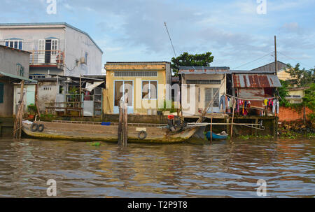 Can Tho, Vietnam - am 31. Dezember 2017. Ein altes hölzernes Boot neben drei kleinen Häusern, die auf einer Wasserstraße in der Nähe von Can Tho im Mekong Blick Günstig Stockfoto