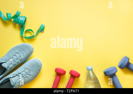 Ein Fitnesscenter mit Hanteln, Maßband, fitness Schuhe, Flasche Wasser auf druckvolle gelben Hintergrund. Ansicht von oben, Platz für Ihren Text. Stockfoto