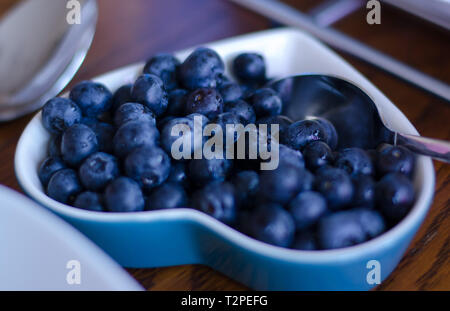 Frische Heidelbeeren in Gruppe in eine kleine Schüssel mit dem Löffel darin platziert. Stockfoto