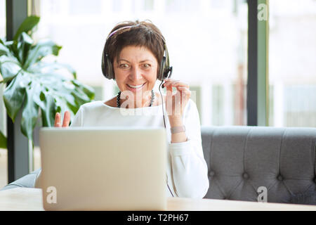 Happy Customer Service Representative. Schockiert, reife Frau am Computer die Hand in die Luft betäubt drinnen halten Sie Kopfhörer mit Hand. Kopieren Stockfoto