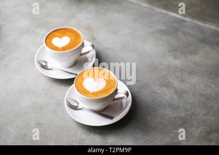 Zwei weiße Tassen leckeren Cappuccino mit Liebe Kunst latte. Valentine's Konzept. Konkrete grauen Hintergrund. Stockfoto