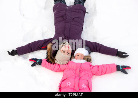 Mutter und Tochter machen Schnee Engel Stockfoto