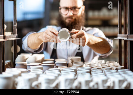 Kreative Mitarbeiter Kontrolle der Qualität der Tonkrüge im Lager mit vielen keramischen Produkte der Töpferei shop Stockfoto