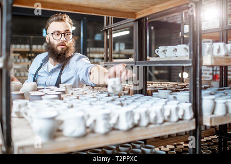 Kreative Mitarbeiter Kontrolle der Qualität der Tonkrüge im Lager mit vielen keramischen Produkte der Töpferei shop Stockfoto