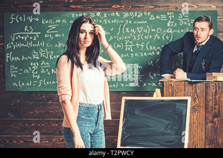 Junge Schülerin in rosa Strickjacke und Blue Jeans stand vor der grünen Platine. Brunette teenage Mädchen im Klassenzimmer hören Erläuterung Stockfoto