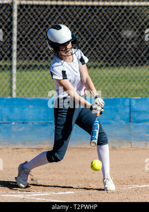 High School weiblichen Softball Spieler in weiße Uniform, die Kontakt mit Ball und Schläger während des Spiels. Stockfoto