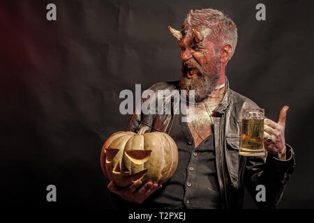 Halloween Urlaub Feier und Party. Mann mit satan Hörner halten Kürbis. Schlechte Gewohnheiten und sucht Konzept. Hipster Dämon Bier trinken auf Schwarz backgr Stockfoto
