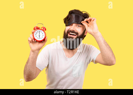 Happy bärtiger Mann mit schlafbrille und Wecker auf gelbem Hintergrund, Konzept Guten Morgen Stockfoto