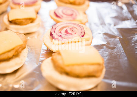 Mini Chicken Burger mit Käse werden auf eine silberne Folie gelegt, bevor sie in den Ofen gelegt wird; Stockfoto