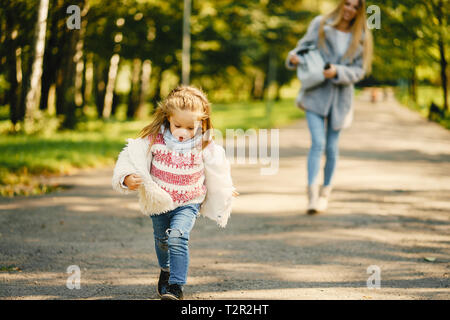 Junge blonde Mutter hinter ihr super energetische toddler Tochter in einem sonnigen Park Stockfoto