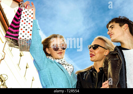 Glückliche junge zwei Business Mädchen Blondinen in Gläsern und einer brunet Kerl zu Fuß die Straße runter und genießen Sie Shopping, Shopping Taschen, Geschenke in ihren Händen. Consu Stockfoto