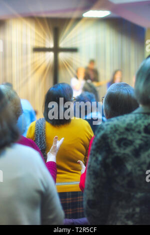 Christliche Gemeinde Gottesdienst gemeinsam Gott, mit Kreuz mit Lichtstrahlen im Hintergrund Stockfoto