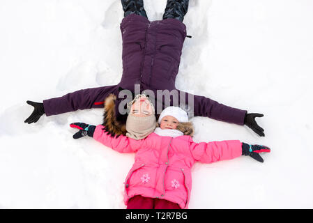 Mutter und Tochter machen Schnee Engel Stockfoto