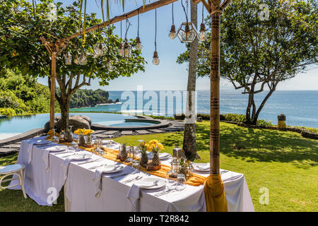 Weiß gedeckten Tischen für Hochzeit Abendessen mit gelben Rosen, Chrysanthemen, Ananas und Glas Lampen eingerichtet. Blick auf den Ozean Stockfoto
