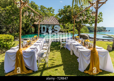 Weiß gedeckten Tischen für Hochzeit Abendessen mit gelben Rosen, Chrysanthemen, Ananas und Glas Lampen eingerichtet. Blick auf den Ozean Stockfoto