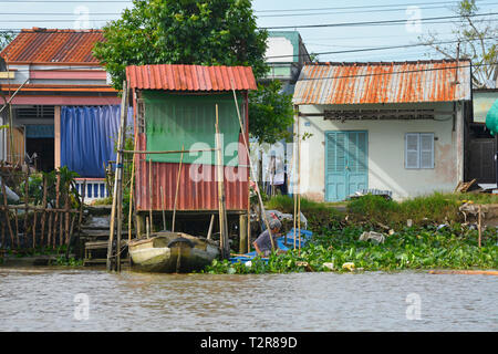 Can Tho, Vietnam - am 31. Dezember 2017. Ein Mann schiebt seinen Ruderboot durch die Vegetation der Ufer auf der Rückseite seines Hauses auf einer Wasserstraße Stockfoto