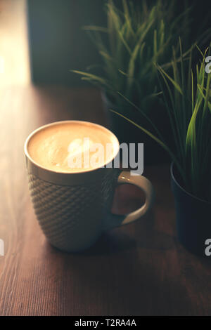 Tasse Kaffee, latte Art mit einem Herzförmigen Muster in einem gemütlichen Cafe am Fenster unter den Pflanzen Stockfoto