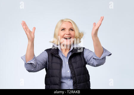 Glücklich und freundlich lächelnde ältere Frau heben die Hände hoch für positives Gefühl und Feier. Positive facial Emotion. Stockfoto