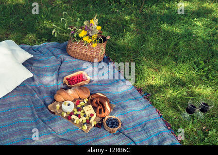 Korb mit Wein und Blumen Brot und Käse auf einem Picknick Decke über grüne Gras auf dem Boden selektiven Fokus Stockfoto