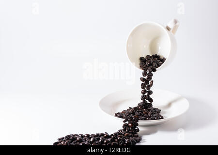Kaffeebohnen gegossen aus Kaffee Tasse mit Untertasse dann auf weisse Oberfläche verschüttetes Stockfoto