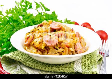 Kohleintopf mit Wurst in eine weiße Platte auf einem Handtuch, Tomaten, Petersilie und eine Gabel auf dem Hintergrund der Holzbretter Stockfoto