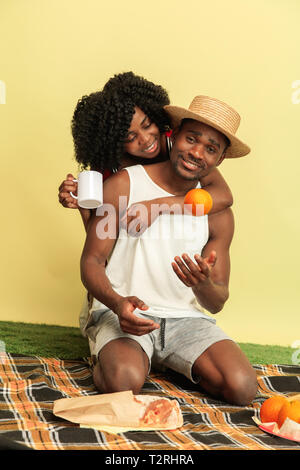 Wundervolle Momente zusammen. Happy African American Family in Picknick gegen gelbe studio Hintergrund. Freizeitaktivitäten, Zweisamkeit, Beziehung und Huma Stockfoto