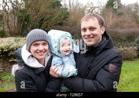 Eltern halten ihr kleines Mädchen mit Blick auf die Kamera Stockfoto