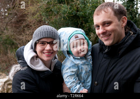 Eltern halten ihr kleines Mädchen mit Blick auf die Kamera Stockfoto