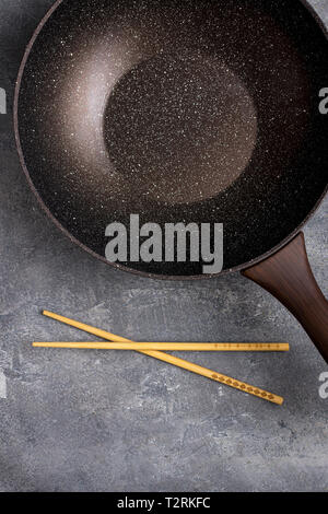 Wok Pfanne leer mit hölzernen Eßstäbchen auf dunklem Hintergrund. Ansicht von oben. Stockfoto