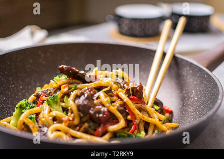 Stir-Fry Udon Nudeln mit Rindfleisch und Gemüse im Wok Pfanne auf dunklem Hintergrund Stockfoto