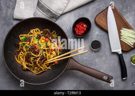 Udon Nudeln mit Rindfleisch und Gemüse Zubereitung im Wok Pfanne auf dunklem Hintergrund Stockfoto