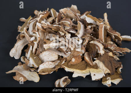 Viele Schichten von trockenen braunen Pilz Boletus Edulis. In Scheiben geschnittene getrocknete Pilze auf schwarzem Hintergrund Stockfoto