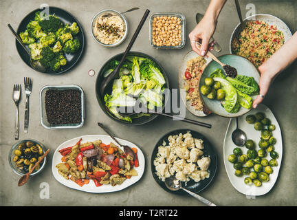 Veganen Abendessen Tabelle einstellen. Gesunde Gerichte in Platten auf Tisch. Flachbild-lay von Gemüse Salate, Hülsenfrüchte, Bohnen, Oliven, Sprossen, Hummus, Frau Hände addi Stockfoto
