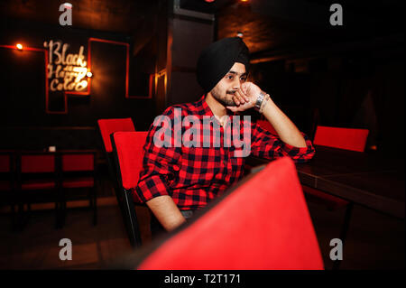 Inder in kariertem Hemd und schwarzen Turban an der Bar sitzen. Stockfoto