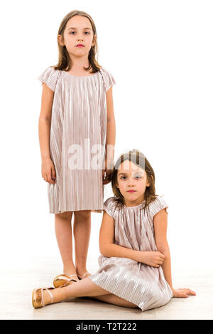 Identische Zwillinge Schwestern sind posieren für die Kamera. Zwillingsschwestern in Kleider betrachten die Kamera mit traurig, langweilig. Vorderansicht, Studio Stockfoto